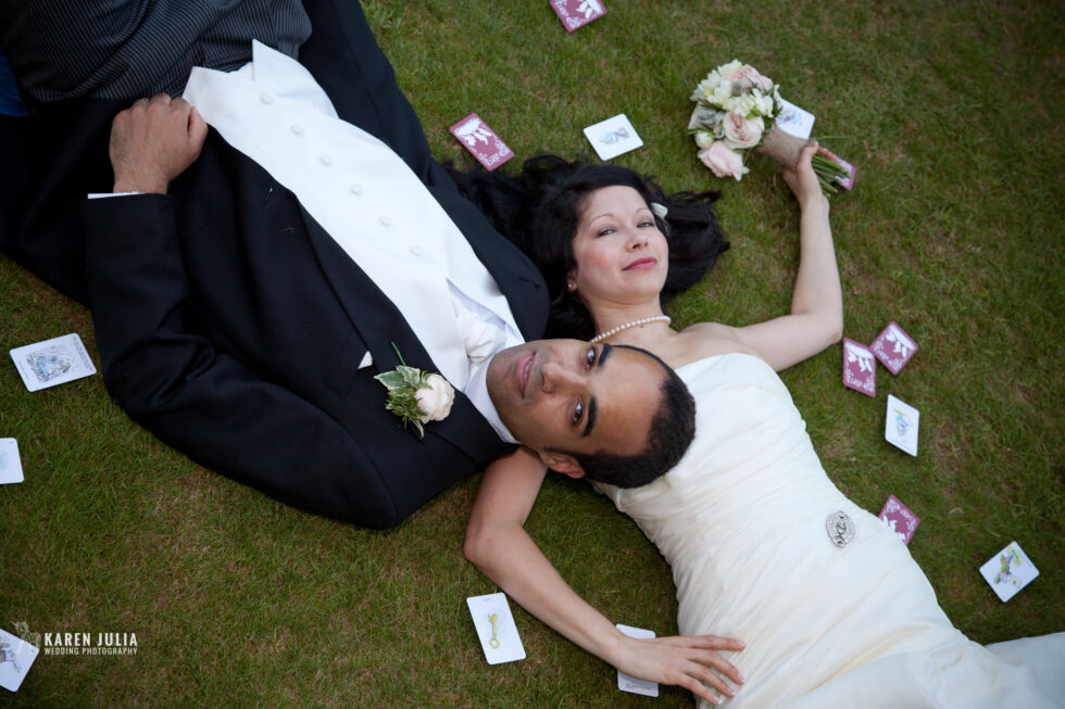 bride and groom lay on the ground surrounded by playing cards at their Alice in Wonderland Wedding