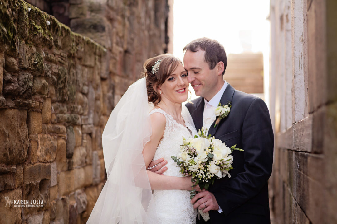 bride and groom embrace in the lane at the side of their town wedding venue