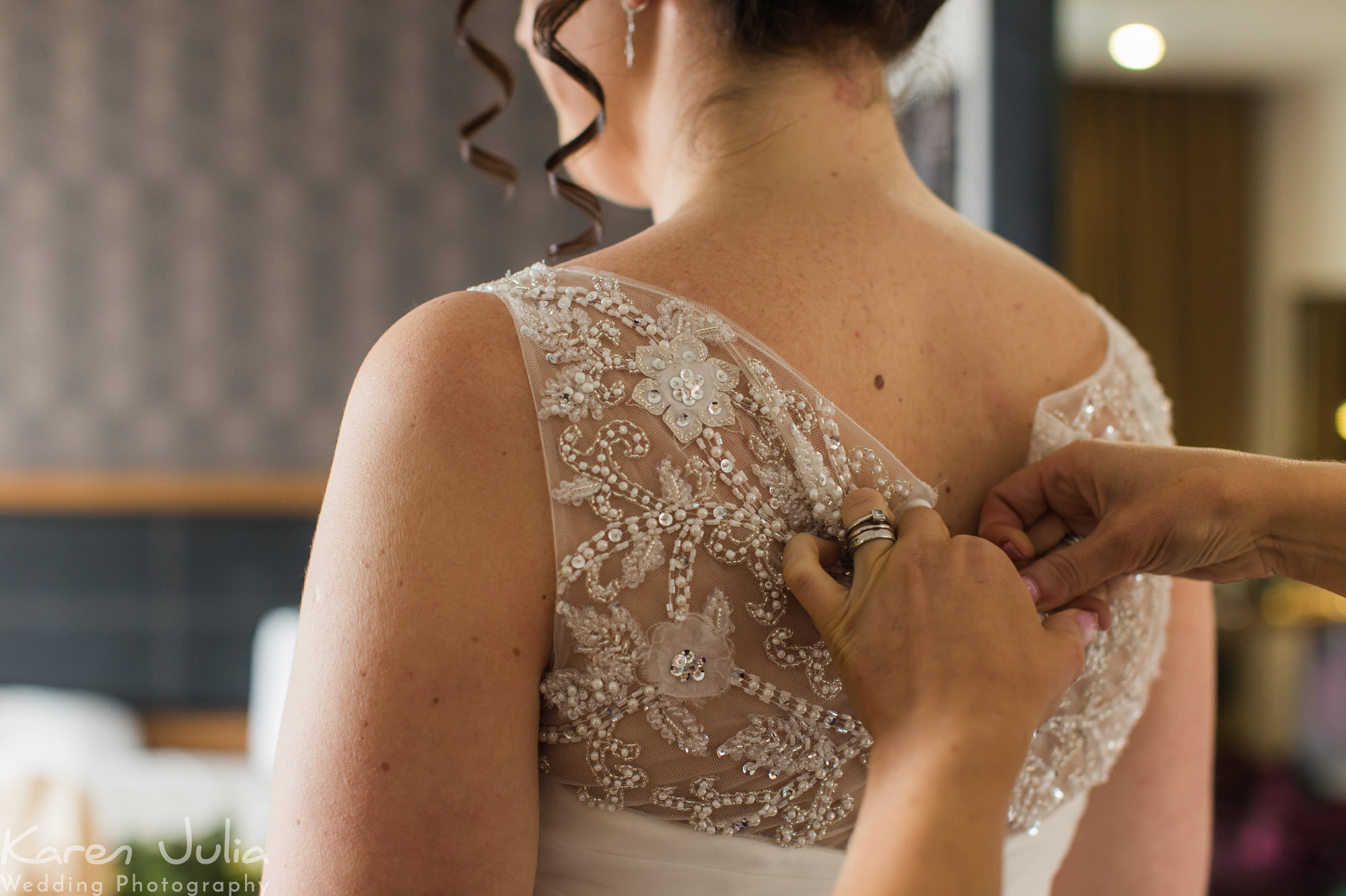 brides mum buttons up her dress on her wedding day