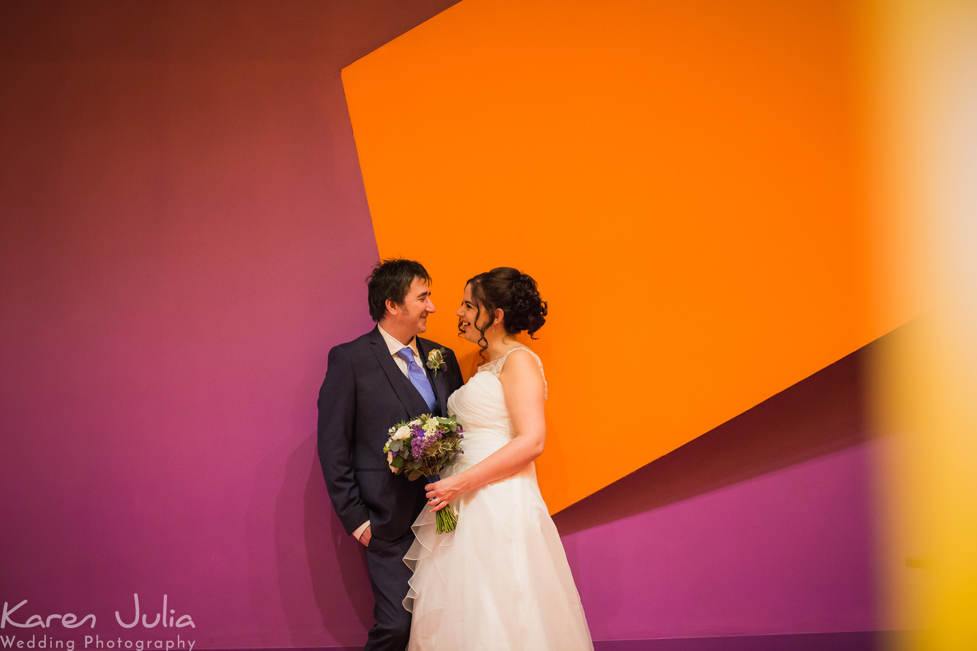bride and groom portrait in front of colourful orange and pink walls in the Lowry Theatre