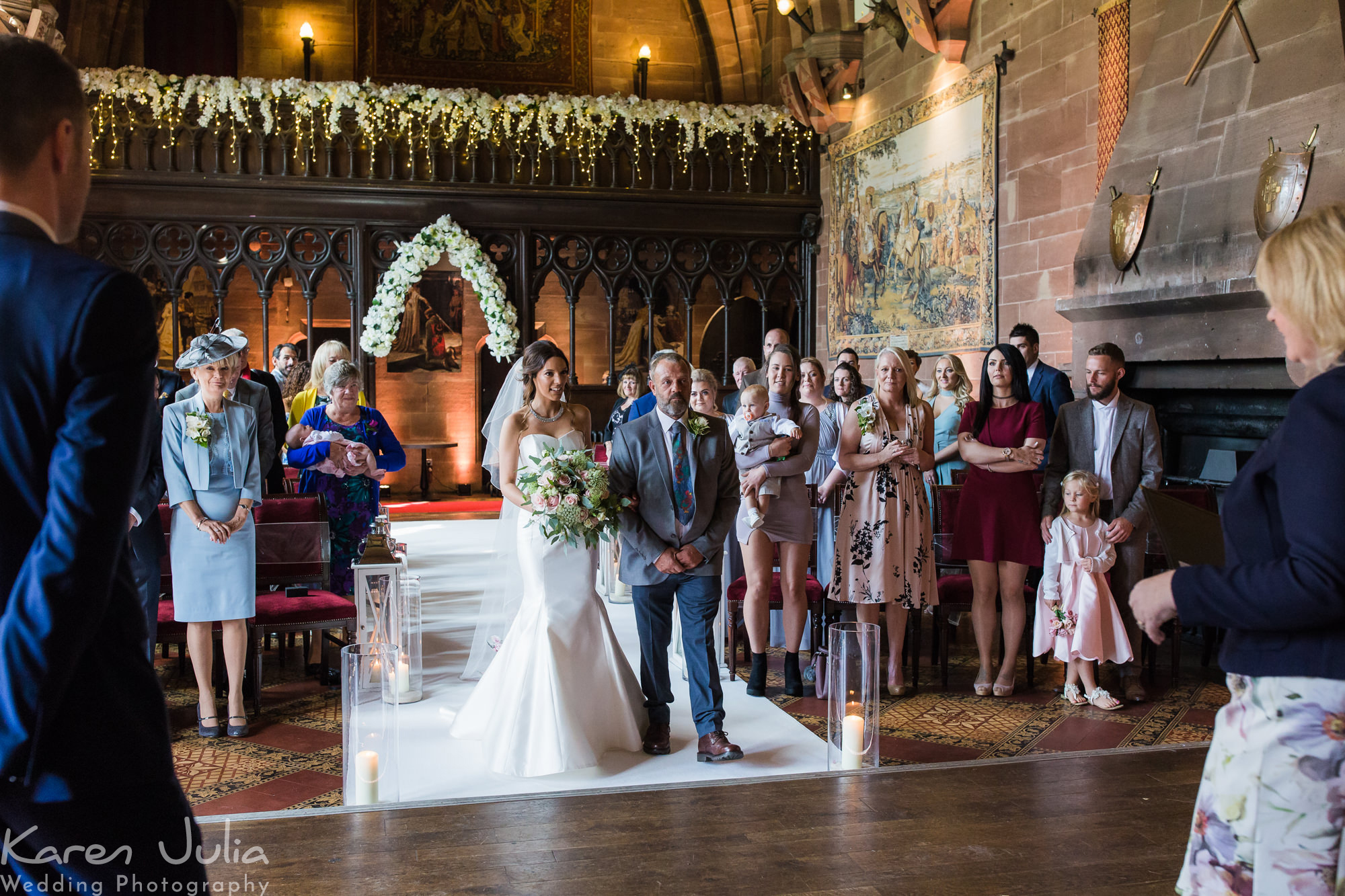 bride walks down the aisle with her Dad in the Great Hall in Peckforton Castle