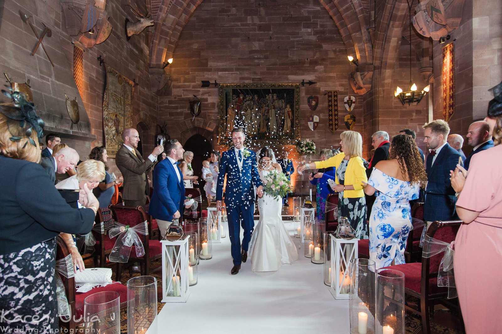 bride and groom walk up aisle whilst guests throw confetti in Peckforton Castle