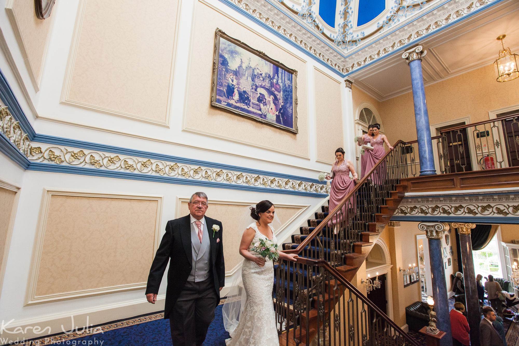 bride and her dad walk down stairs to ceremony, followed by bridesmaids