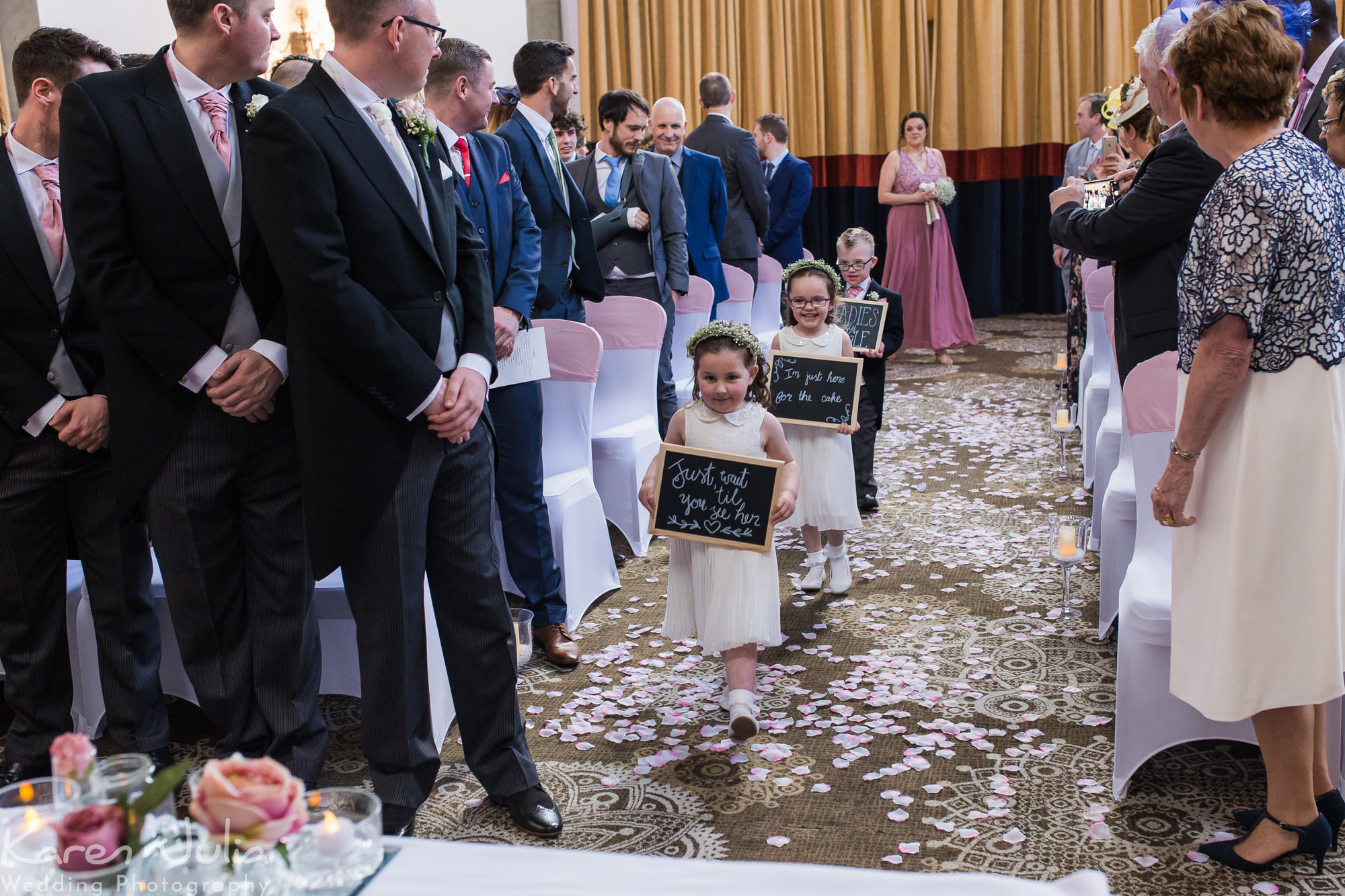 flowers girls walk down aisle carrying signs in the Tilden suite