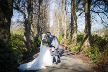 bride and groom kiss in the tree lined walkway in Maxwell Park on their wedding day