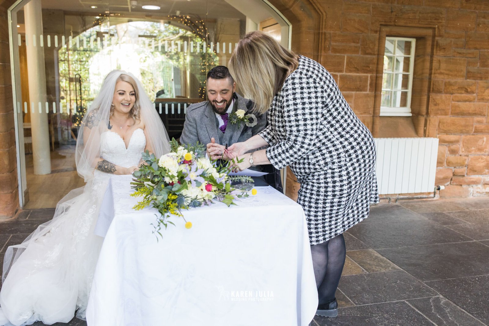 bride and groom take turns to sign the wedding register in Pollockshields Burgh Hall