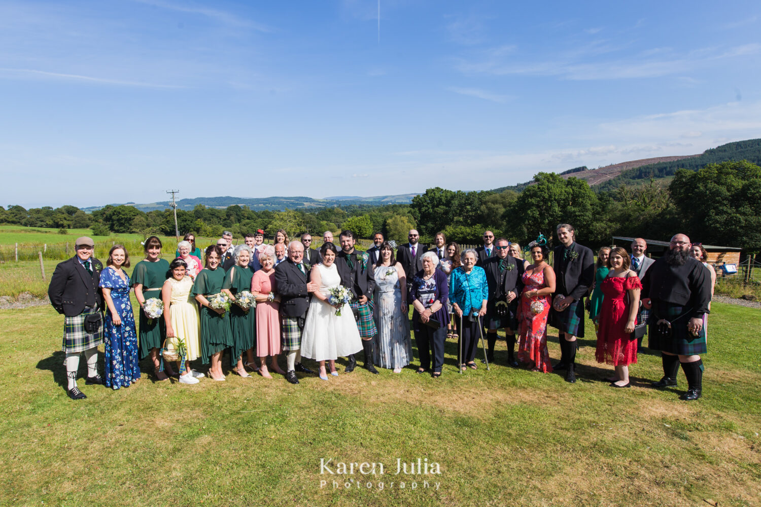 a wedding group photo at Fruin Farm with Loch Lomond in the background