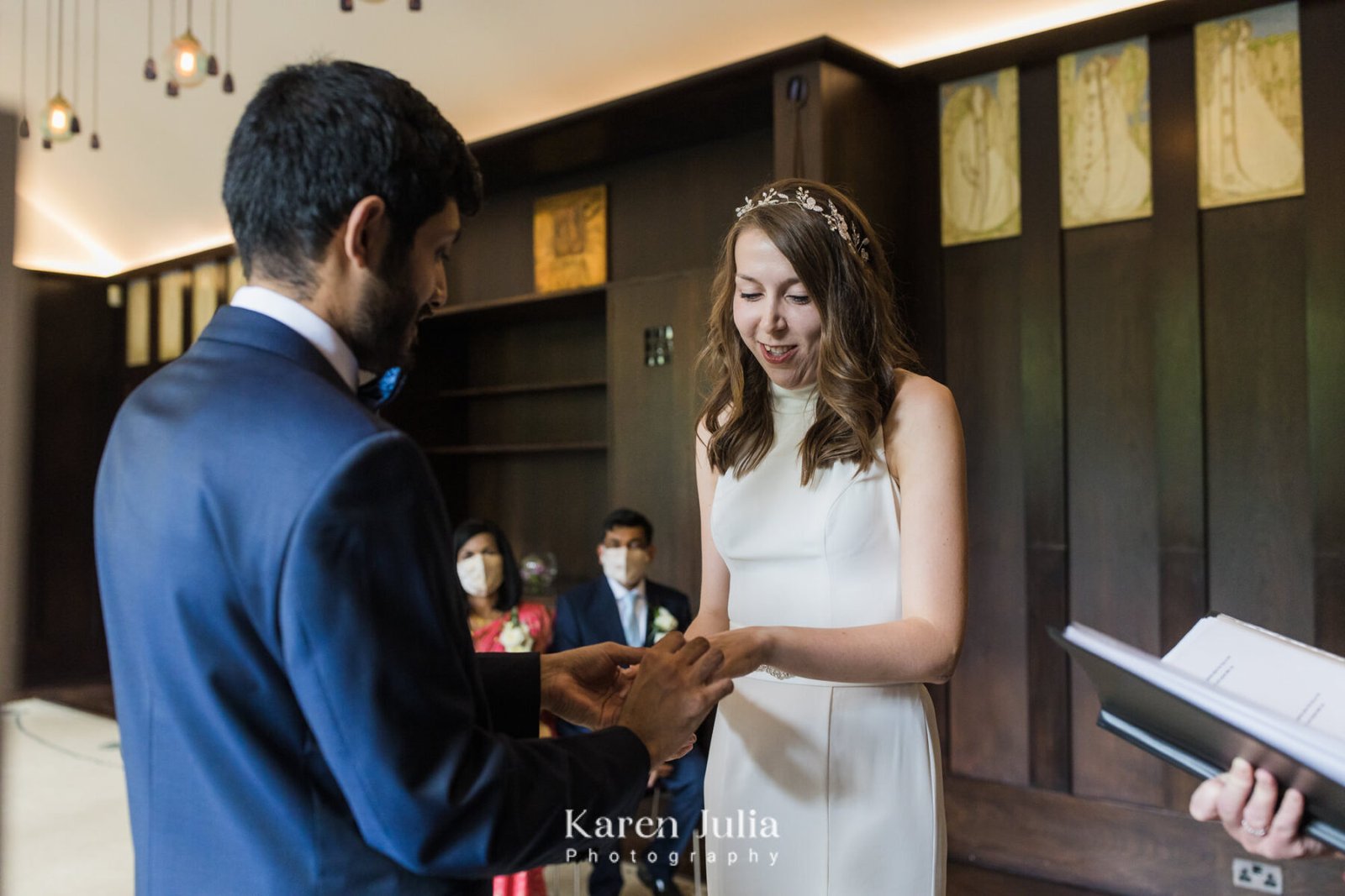 groom places a wedding ring on the brides finger as they say their vows