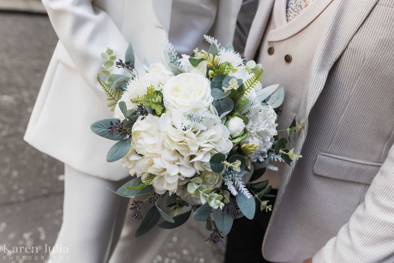 brides ivory bouquet being held in front of her stylish white suit
