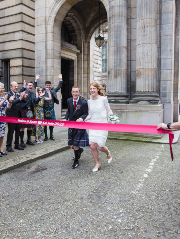 bride and groom run towards a finish line being held out by guests