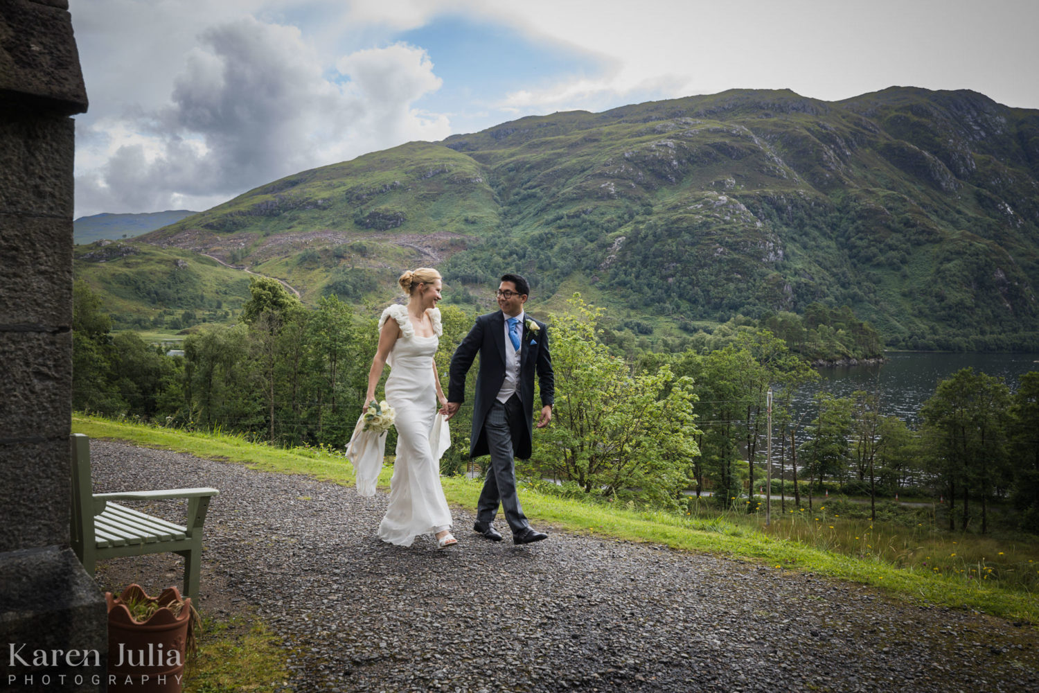 bride and groom walking together next to Glenfinnan Church, with Loch Shiel in the background
