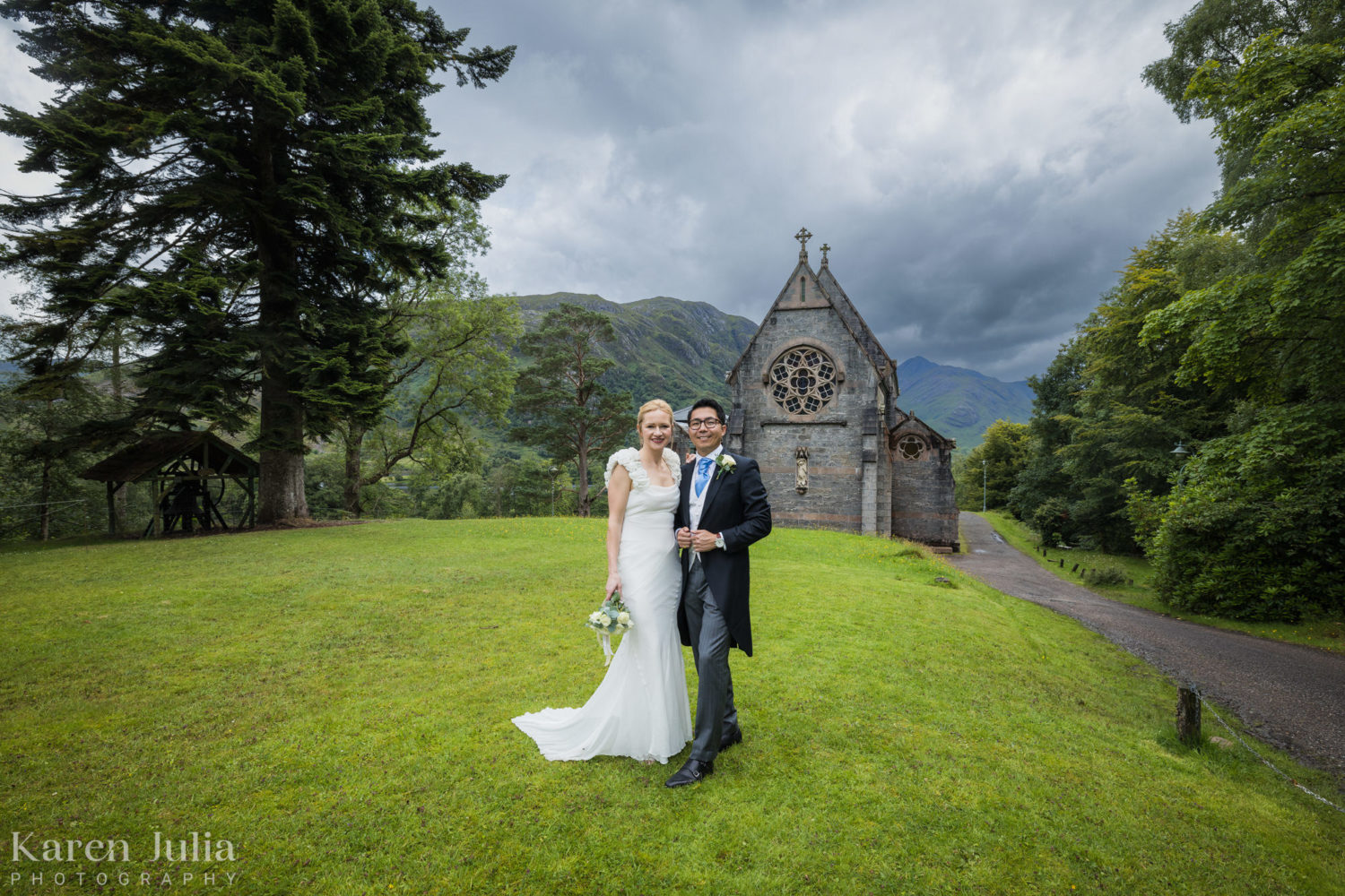 bride and groom pose for a portrait next to St Mary and St Finnan church