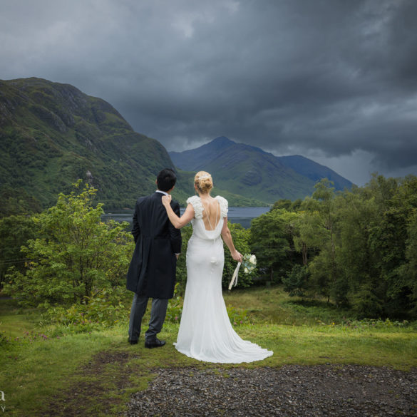 bride and groom standing facing the loch at Glenfinnan during their wedding portraits