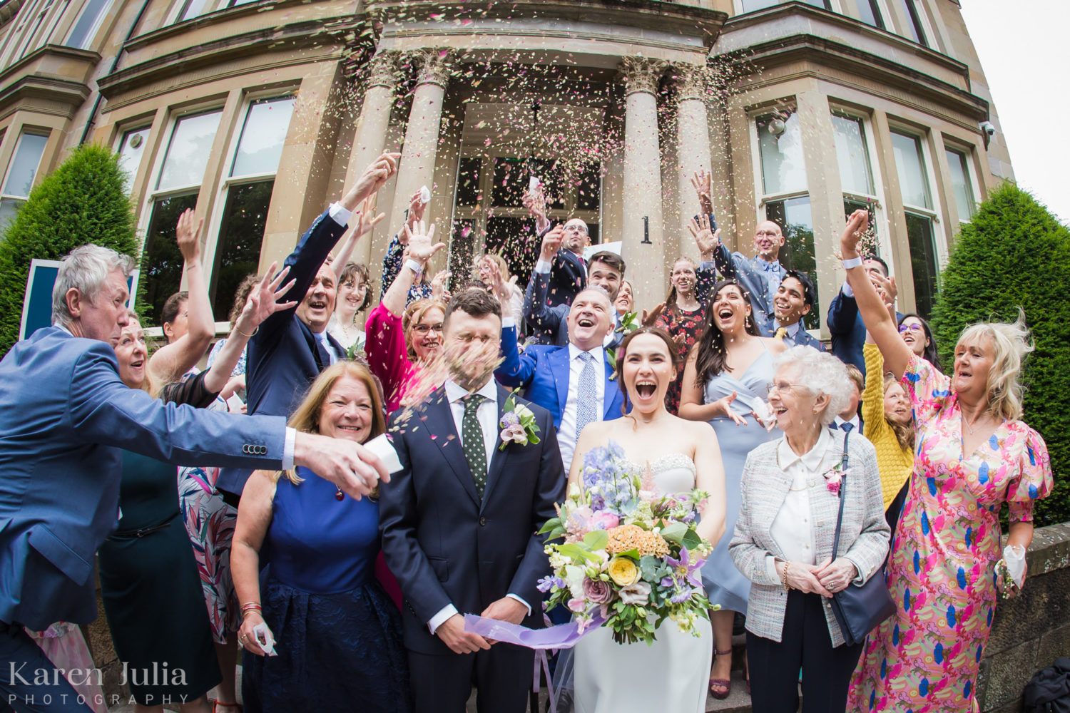 bride and groom surrounded by guests during confetti throw on the stairs at One Devonshire Gardens