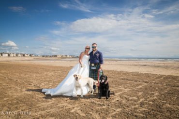 bride and groom pose for a couple portrait on Ardrossan south beach with their dogs