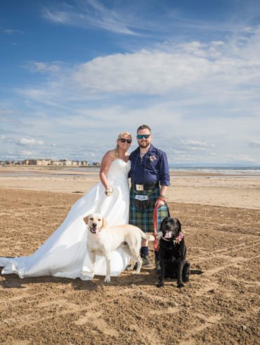 bride and groom pose for a couple portrait on Ardrossan south beach with their dogs