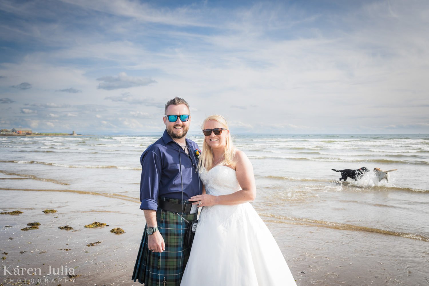 bride and groom on Ardrossan south beach in their wedding attire with their dogs