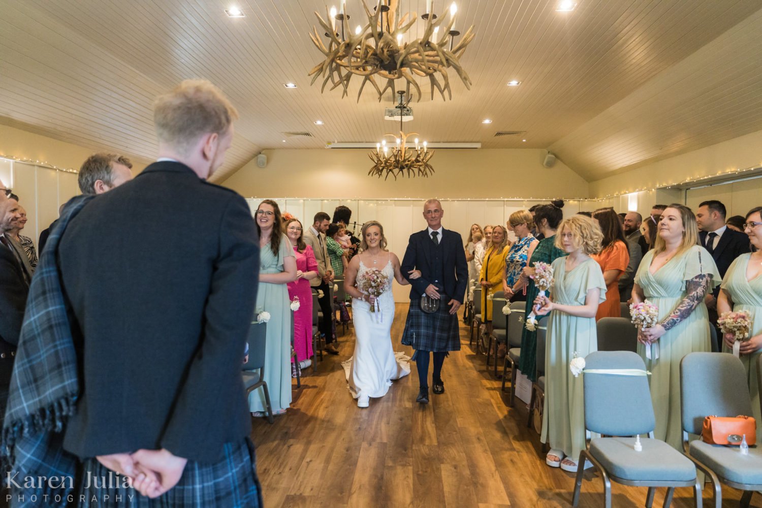 bride walks down the aisle to meet her groom at Loch Lomond Arms hotel in Luss