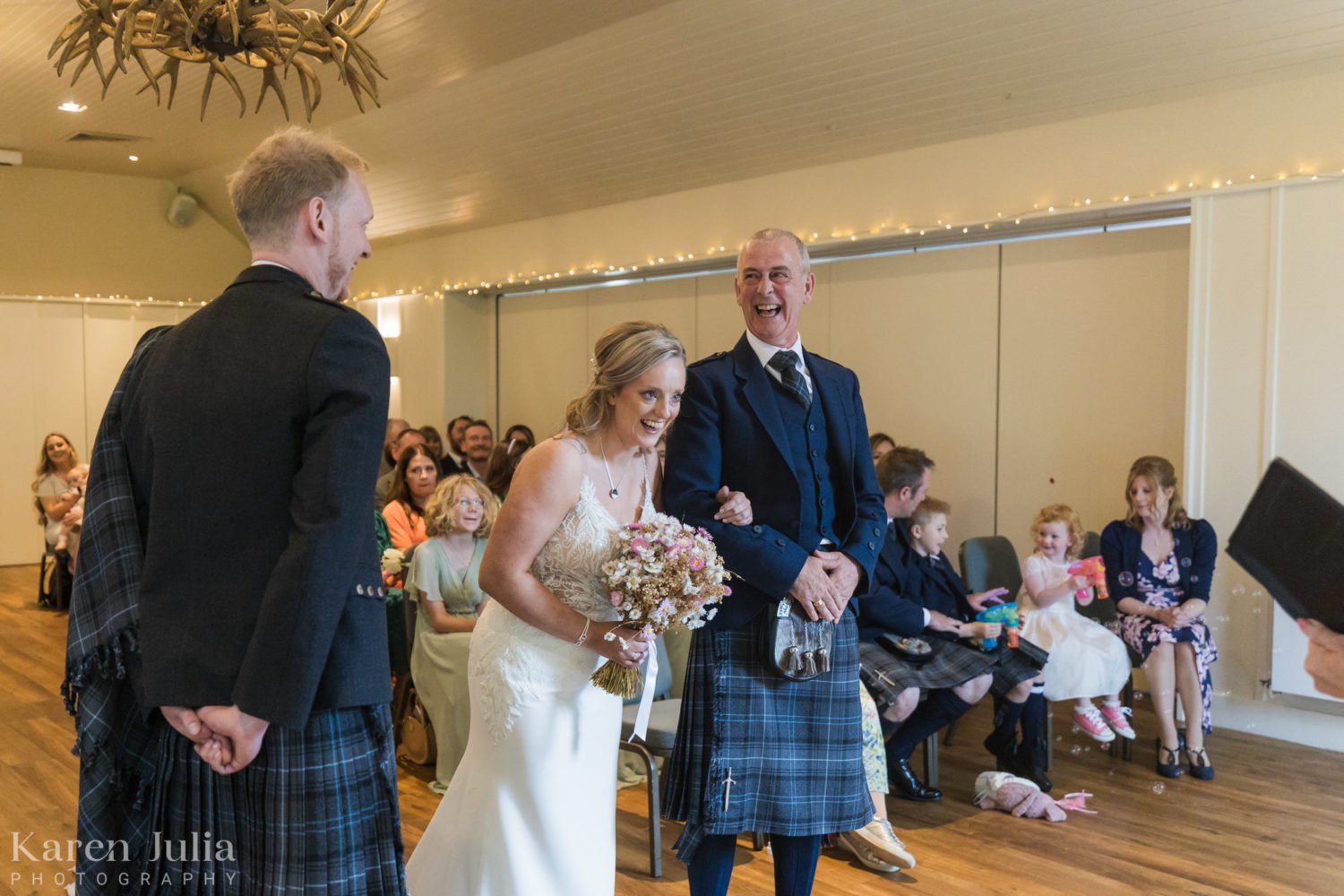 bride and her dad arm in arm and laughing during the wedding ceremony at Loch Lomond Arms